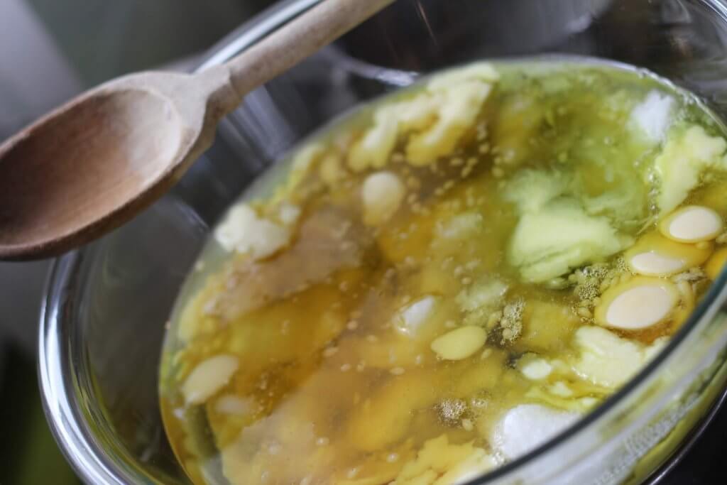 Foot and Heel Salve melting in glass bowl with wooden spoon on the side.