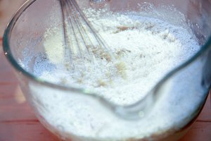 Powders being incorporated into melted oils, butters, and wax with whisk in bowl.