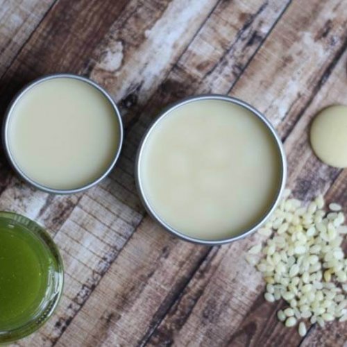 Overhead view of cracked feet and heel salve in metal containers with raw ingredients on the table around the product.